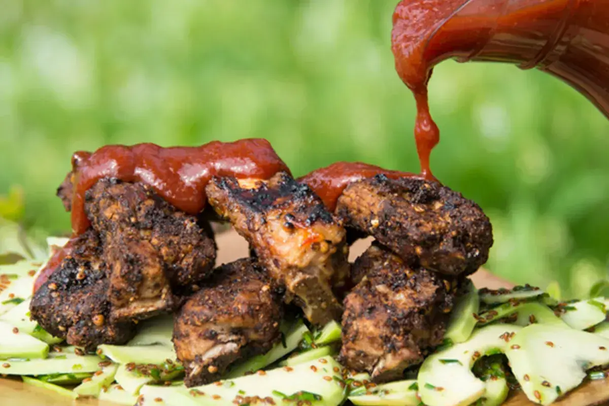 Grillade revbensspjäll toppas med en generös mängd röd bbq sås, serverade på en bädd av gurksallad.