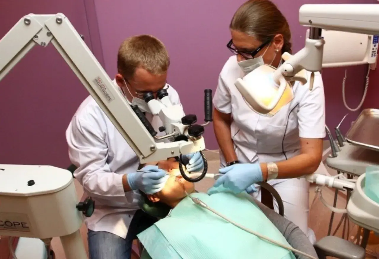 Dentysta i asystentka pracują przy pacjencie pod mikroskopem stomatologicznym.