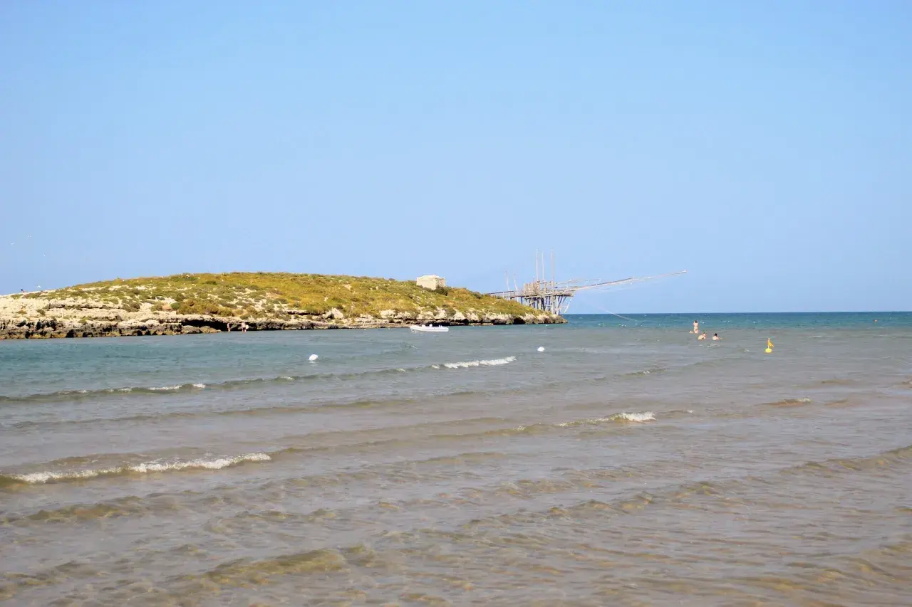 La chianca di Vieste, con la sua struttura in legno sul mare, si staglia contro il cielo azzurro. L'acqua cristallina invita a un bagno rinfrescante.