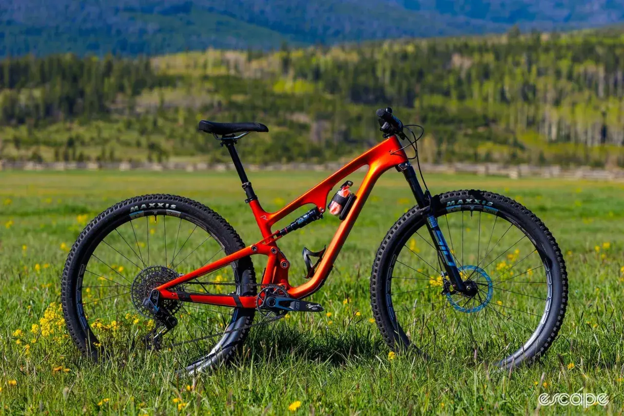 An orange Revel Ranger V2 mountain bike sits in a grassy field, ready for adventure. This revel ranger v2 review shows its sleek design.