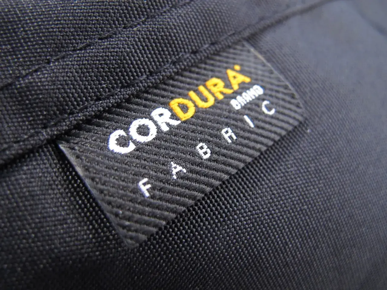 Czarna tkanina z naszywką "CORDURA FABRIC". Materiał ten, znany ze swojej wytrzymałości, często wykorzystywany jest w produktach outdoorowych, jak plecaki czy torby.