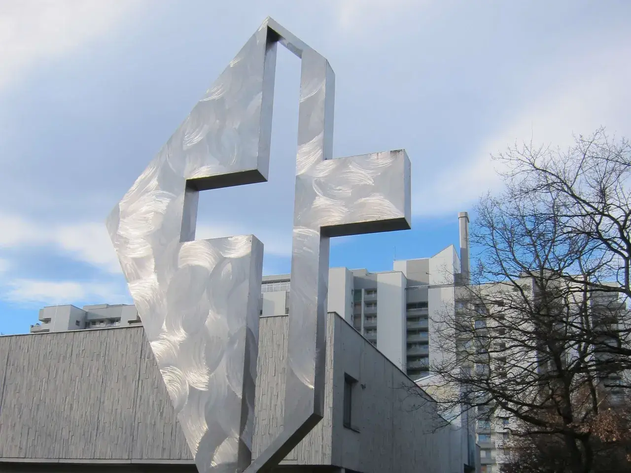 Modernes Kreuz aus gebürstetem Metall vor der Kirche St. Lukas Westkreuz.