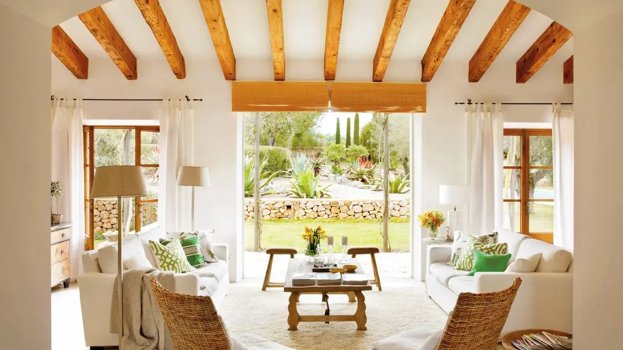 Salón con vigas de madera y vistas a un jardín exuberante, reflejo de la arquitectura mediterránea.