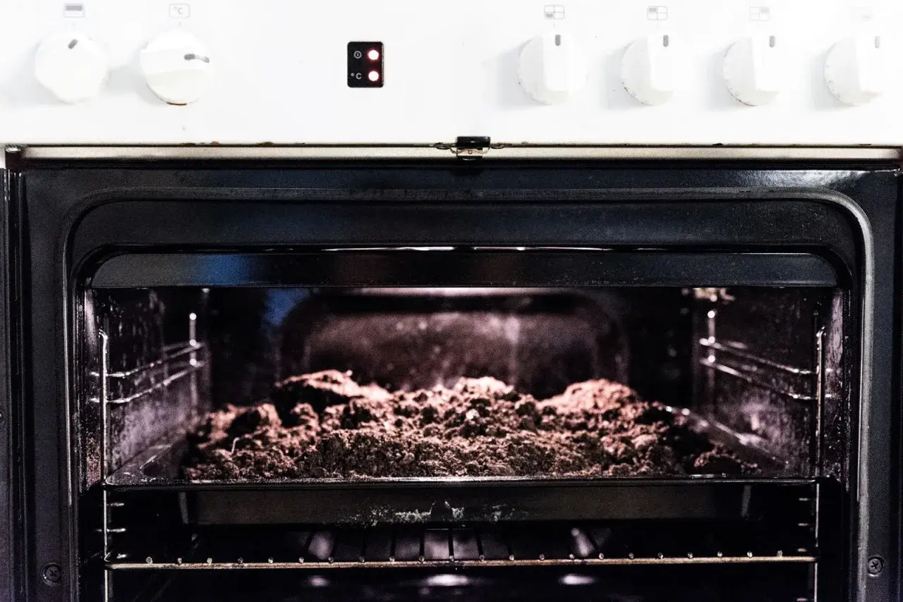 An open oven with a baking tray filled with soil on the rack.