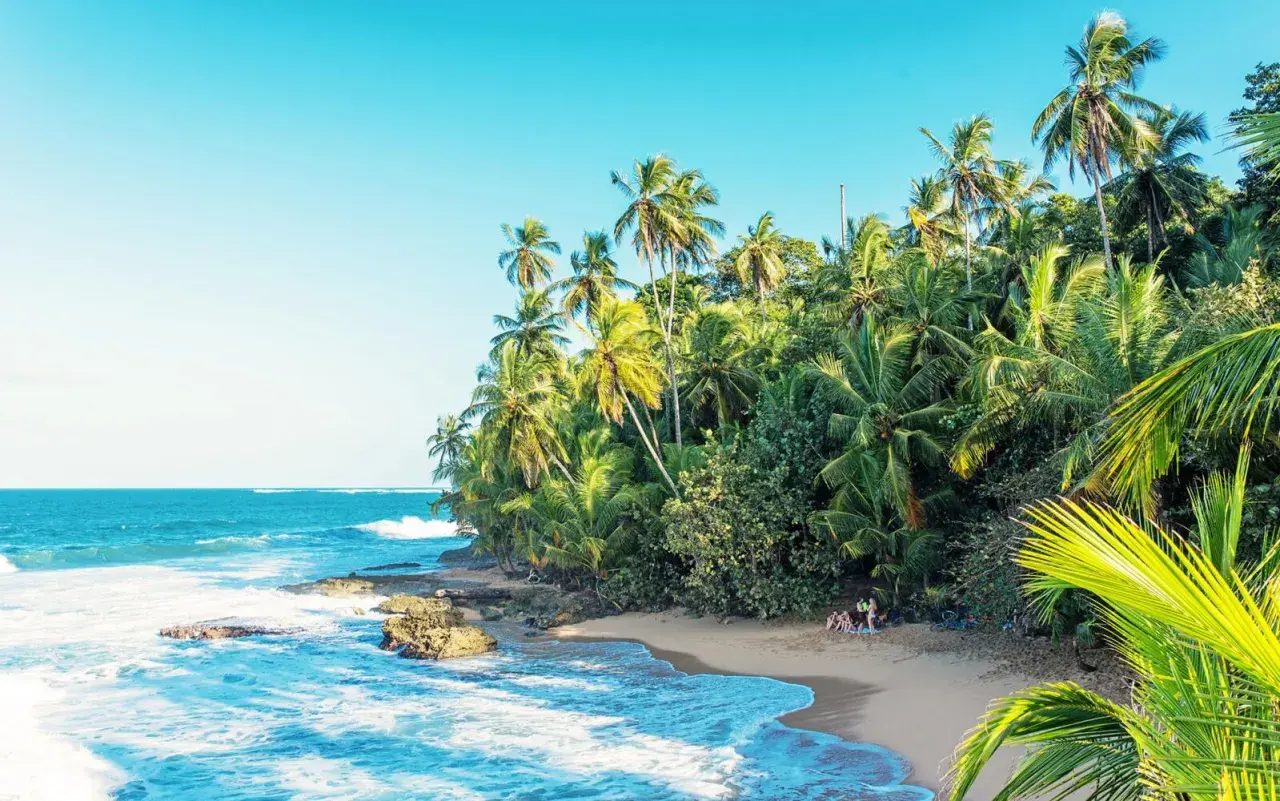 En tropisk strand i Costa Rica med vajande palmer, turkost hav och en liten grupp människor som njuter av solen.