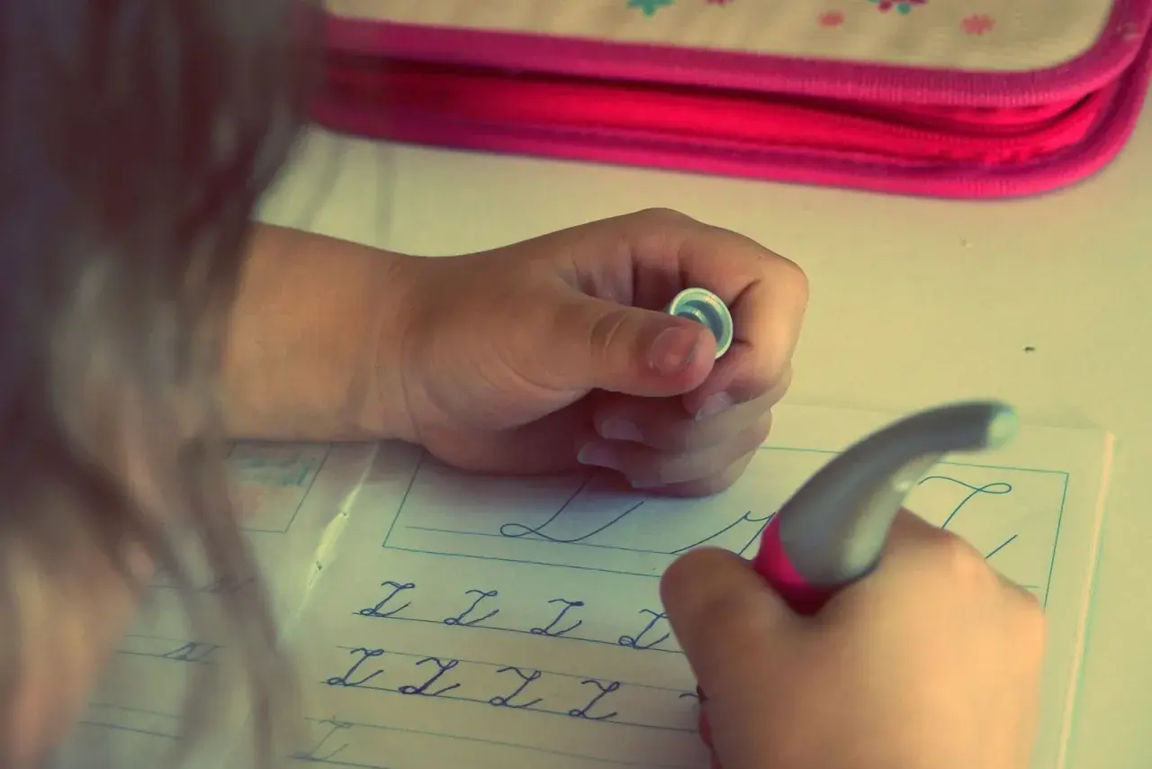 Niño/a practicando caligrafía en un cuaderno con letras cursivas.