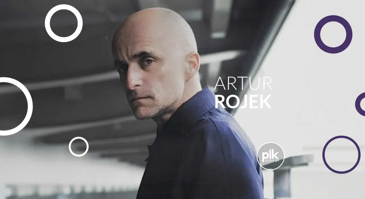 Artur Rojek, znany z energetycznych koncertów, na tle miejskiego krajobrazu.