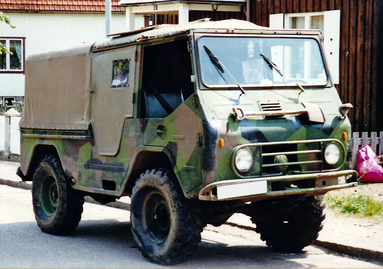 En kamouflerad Volvo L3314 står parkerad framför ett hus.