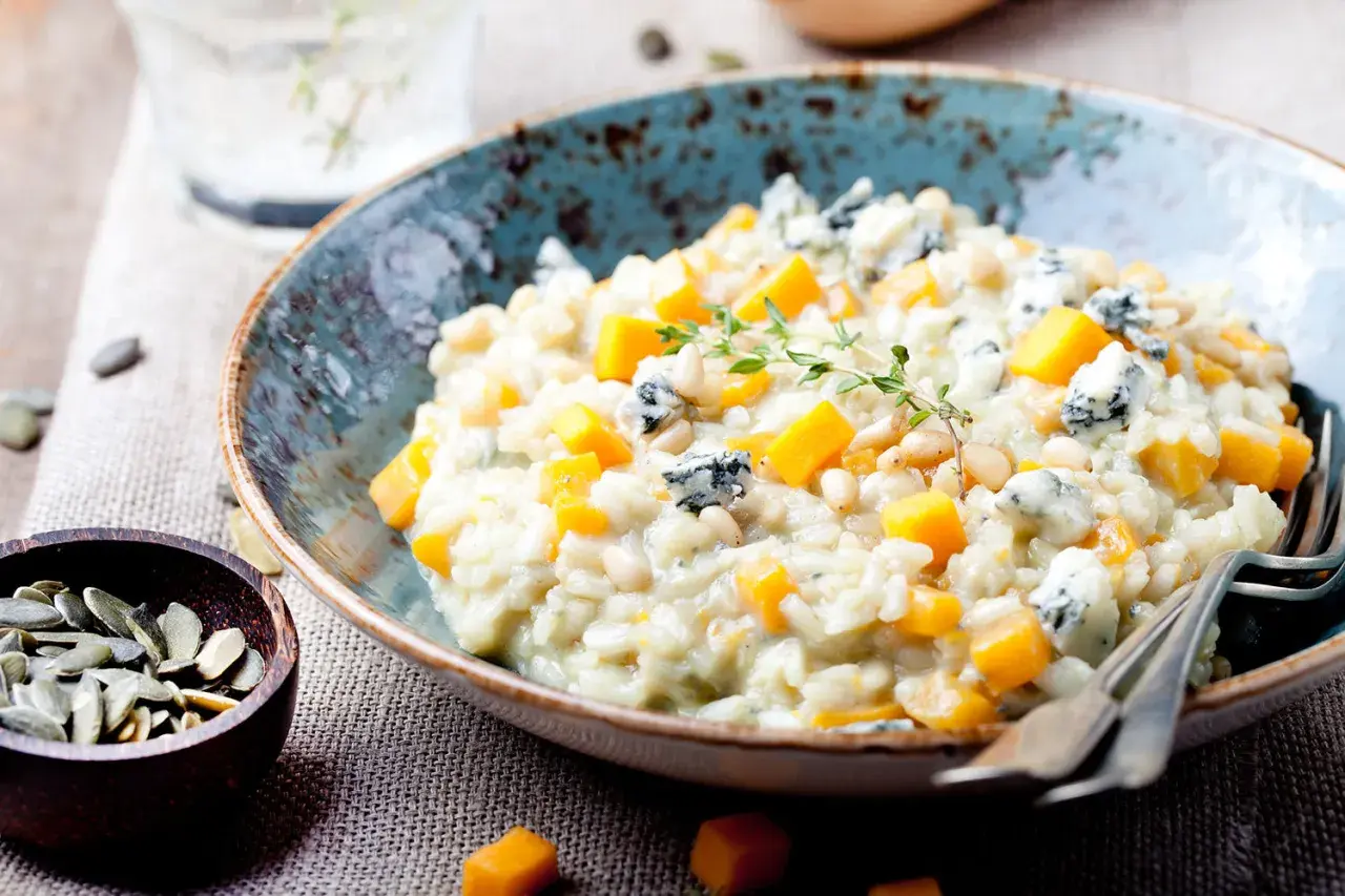 Cremiges Kürbis-Risotto mit Blauschimmelkäse und Pinienkernen. Ein Glas Wasser steht bereit, perfekt zum Genießen dieses Risotto, welcher Wein passt wohl dazu?