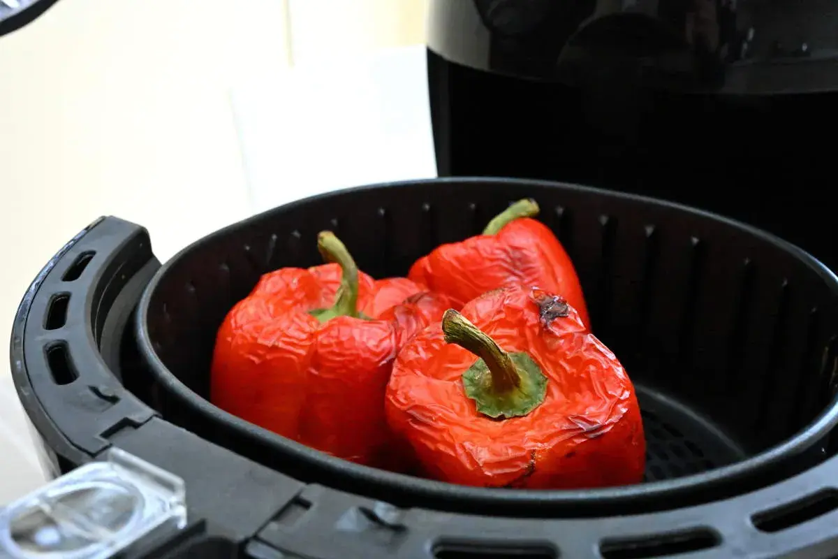Peperoni rossi interi cotti nella friggitrice ad aria, con la buccia leggermente raggrinzita e qualche macchia scura.