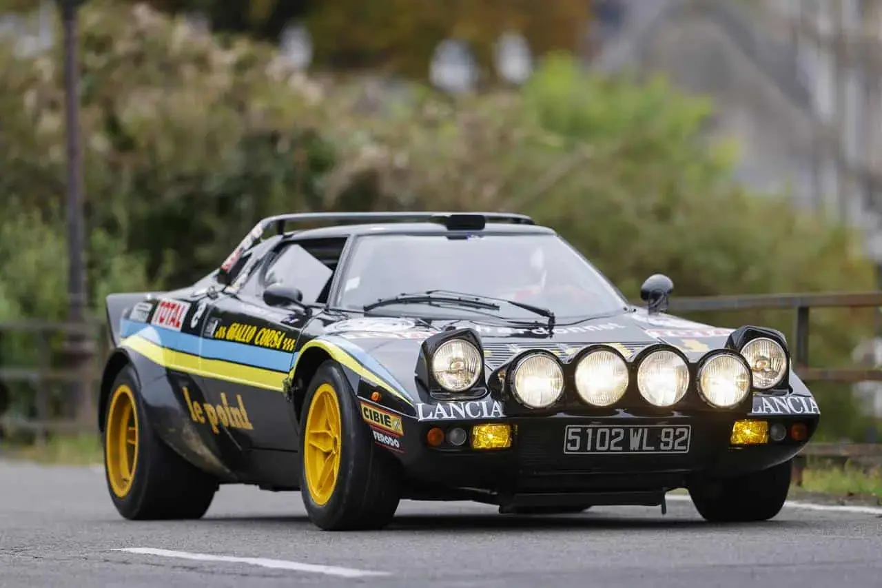 Czarny Lancia Stratos z żółtymi felgami i rajdowymi oznaczeniami, gotowy do pokonania kolejnego zakrętu.