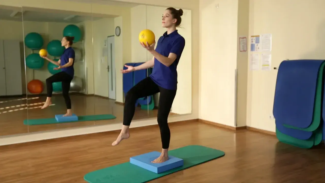 Frau balanciert auf einem blauen Kissen, um zu zeigen, wie einfach arthrose heilen ist. Sie hält einen gelben Ball.
