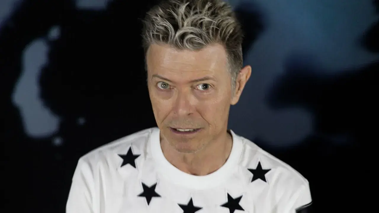 Ikoniczny David Bowie w 2016 roku, w białej koszulce w czarne gwiazdy, z charakterystyczną fryzurą.