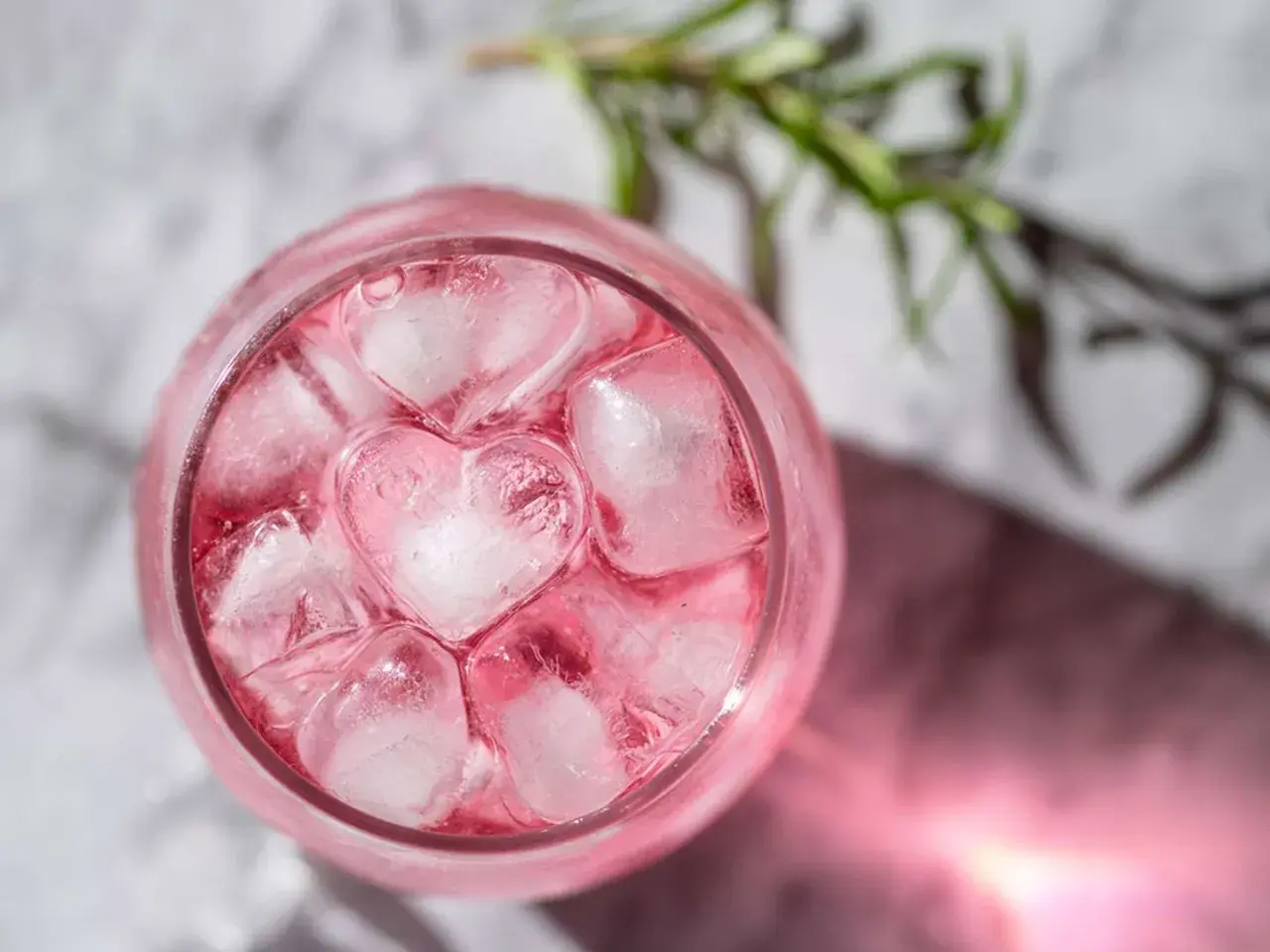 En rosa drink med hjärtformade isbitar och en rosmarinkvist.