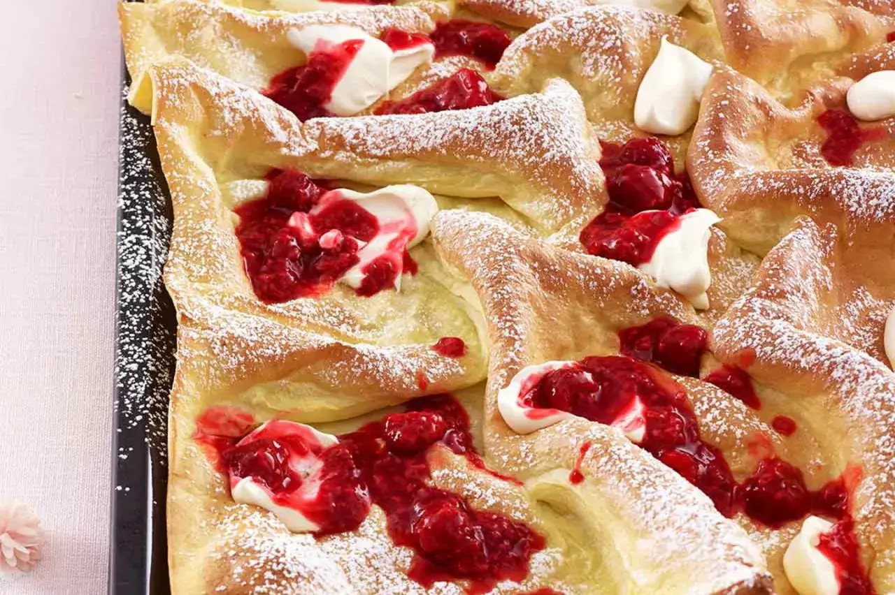 Luftige Pfannkuchen vom Blech, bestäubt mit Puderzucker und garniert mit frischer Himbeersauce und Sahne. Ein Genuss für jeden Anlass!