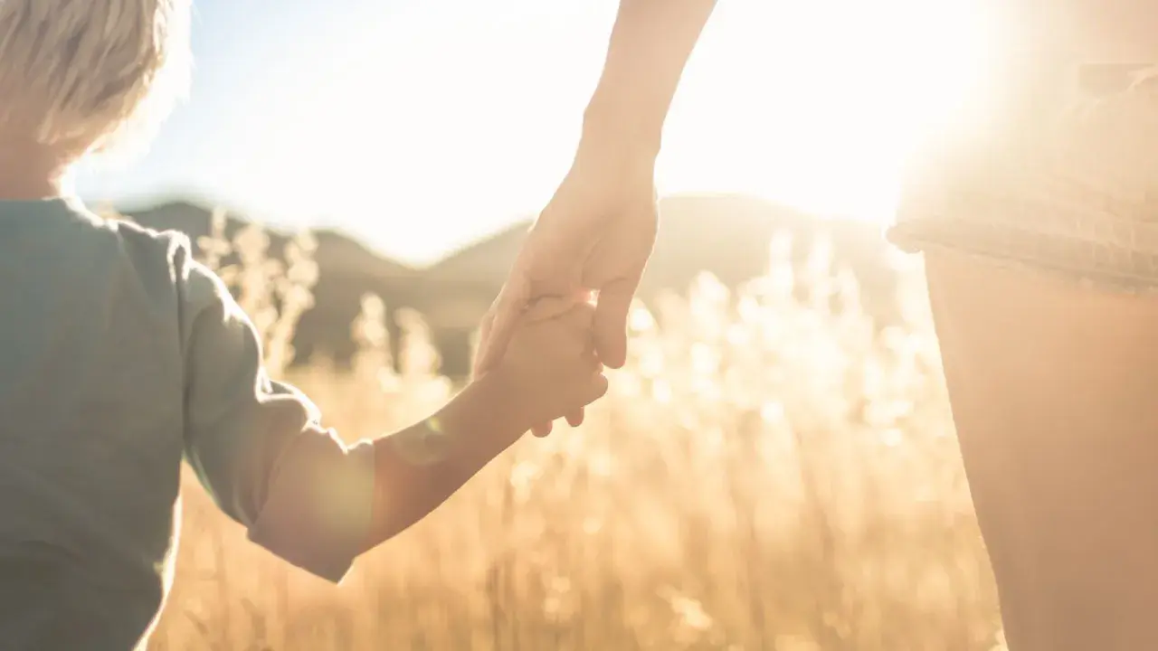 Un niño y un adulto se toman de la mano al atardecer. Pensamientos de orgullosa frases cortas para un hijo varon.