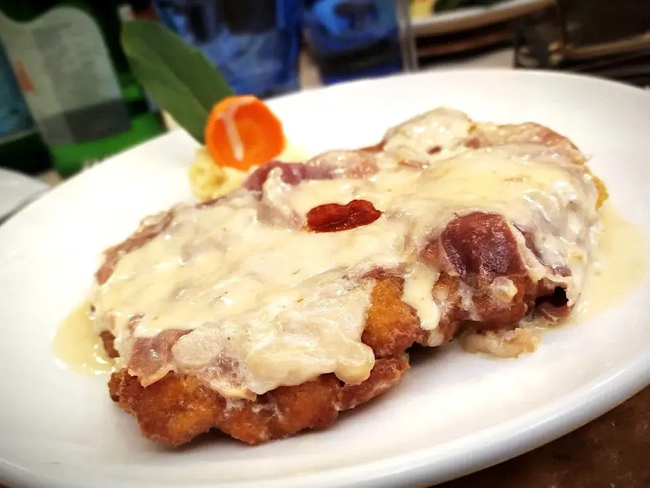 Cotoletta alla bolognese dorata e filante, con prosciutto e formaggio fuso, servita su un piatto bianco.