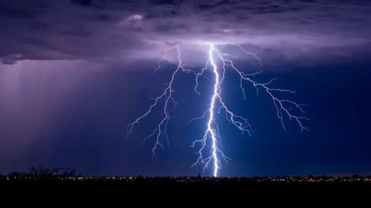 Un rayo ilumina el cielo nocturno, como si fuera un sueño con tormenta. Las nubes púrpuras y el horizonte iluminado por luces de ciudad crean una escena dramática.
