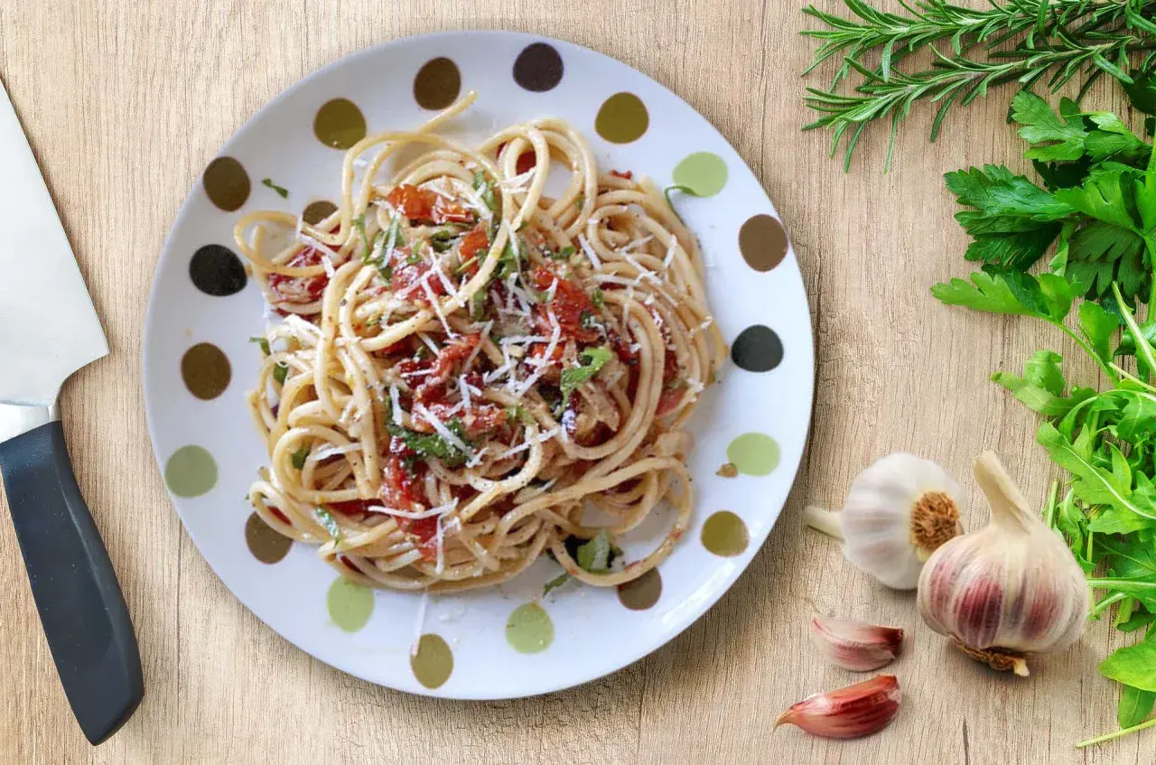 Un plato de espagueti aglio olio peperoncino, con ajo, perejil y un toque de tomate.