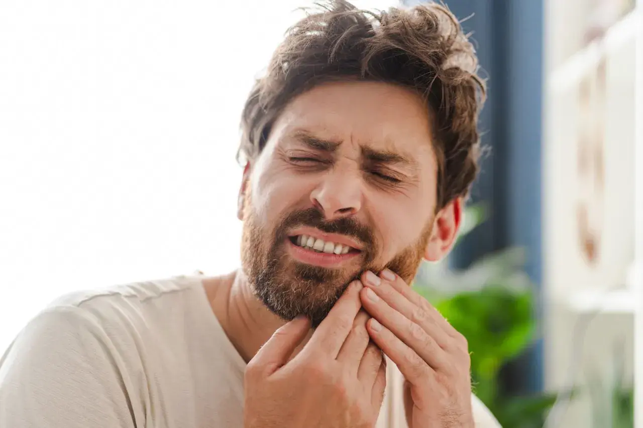 Hombre con expresión de dolor, tocándose la mejilla por una caries muela.