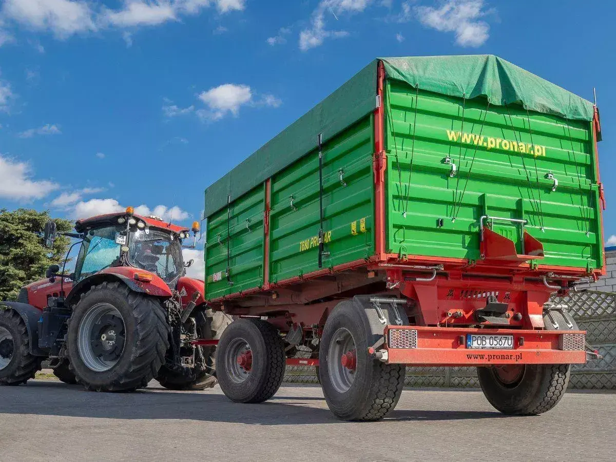 Czerwony traktor ciągnie zieloną przyczepę. Dowiedz się, jakich przyczep nie trzeba rejestrować, by ułatwić sobie pracę w gospodarstwie.