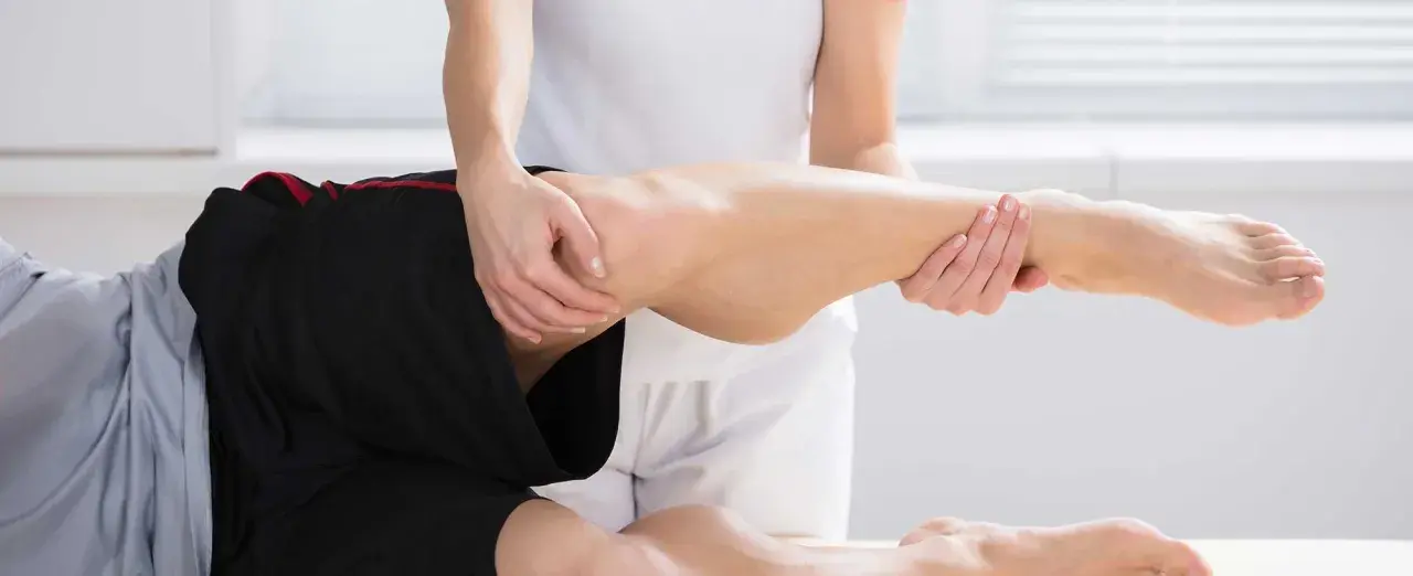 Fizjoterapeuta pomaga pacjentowi z bólem kolca biodrowego, wykonując delikatne ruchy nogą.