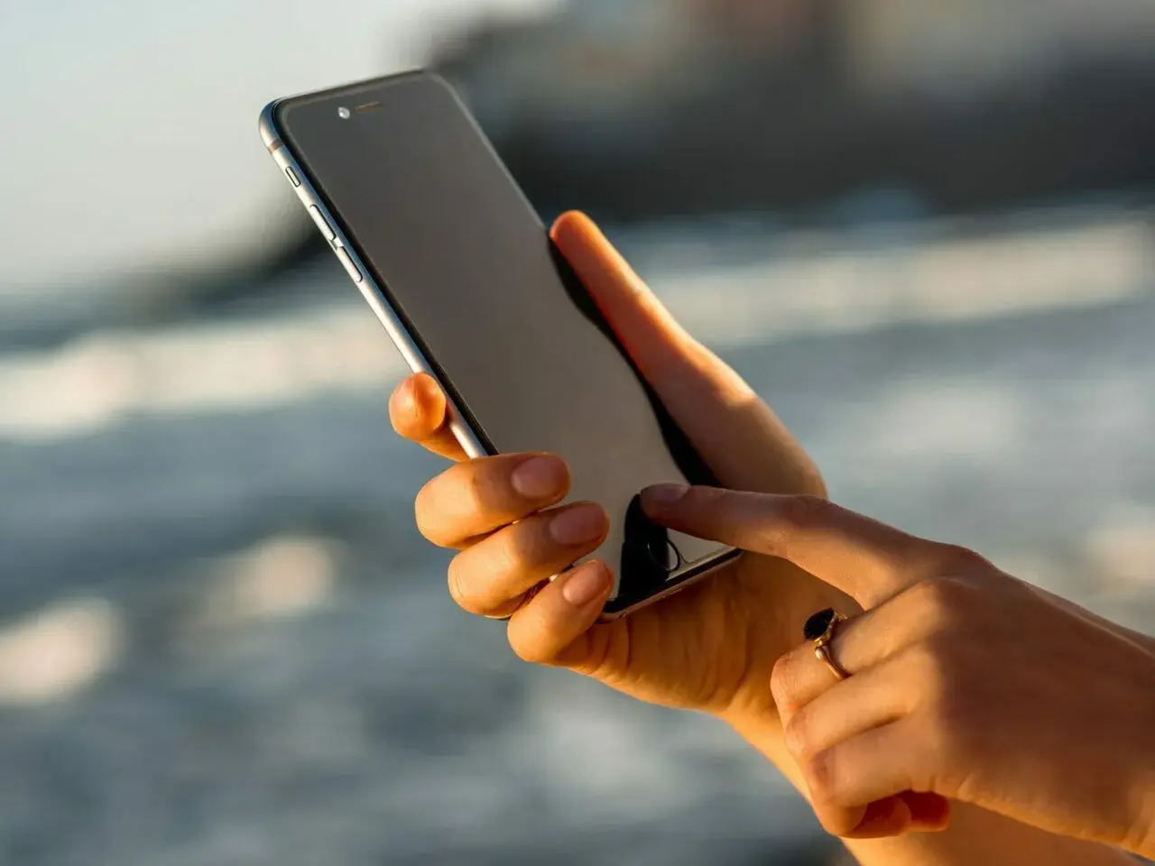 Dłoń z pierścionkiem pokazuje, jak włączyć iPhone'a, dotykając ekranu.