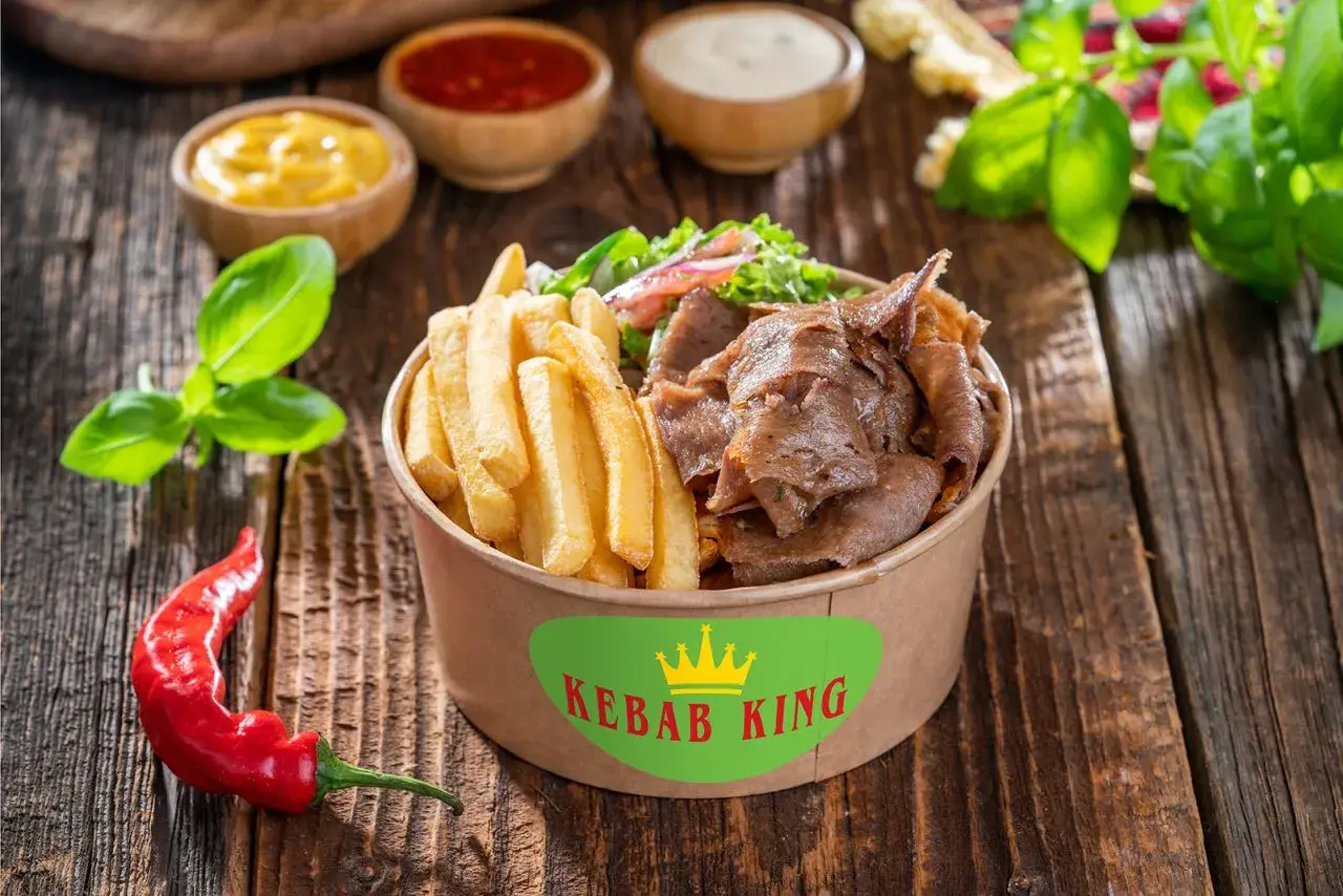 Kebab z frytkami i warzywami w pudełku Kebab King, obok sosów i papryczki chili.
