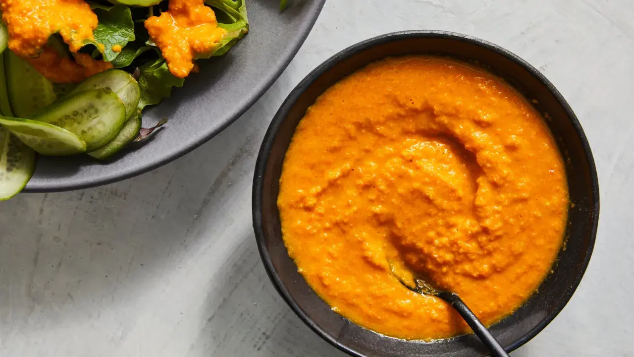 A vibrant bowl of carrot ginger dressing sits next to a salad with cucumber slices.