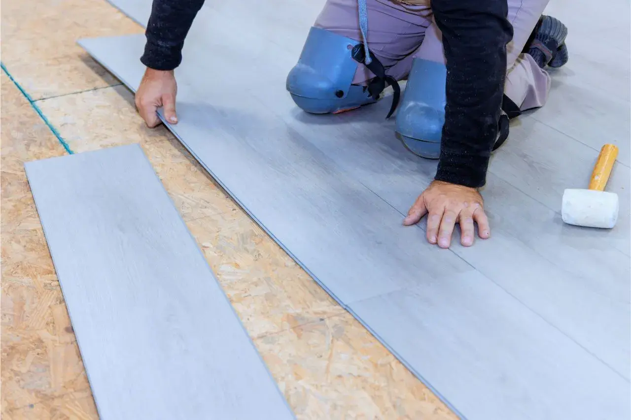 Instalación suelo laminado: un profesional coloca una tabla de suelo laminado gris sobre una base de madera contrachapada.