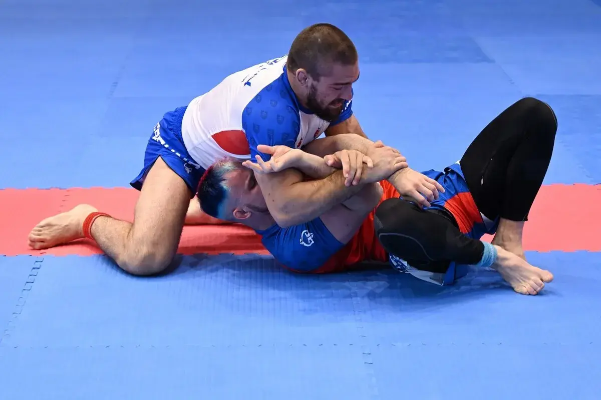 Dwóch mężczyzn walczy na macie. Jeden klęczy, drugi leży. To właśnie bjj co to za sport?