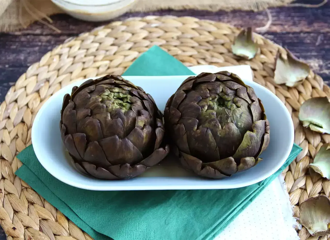 Deux artichauts violets sur une assiette blanche, prêts pour une recette d'artichaut savoureuse.