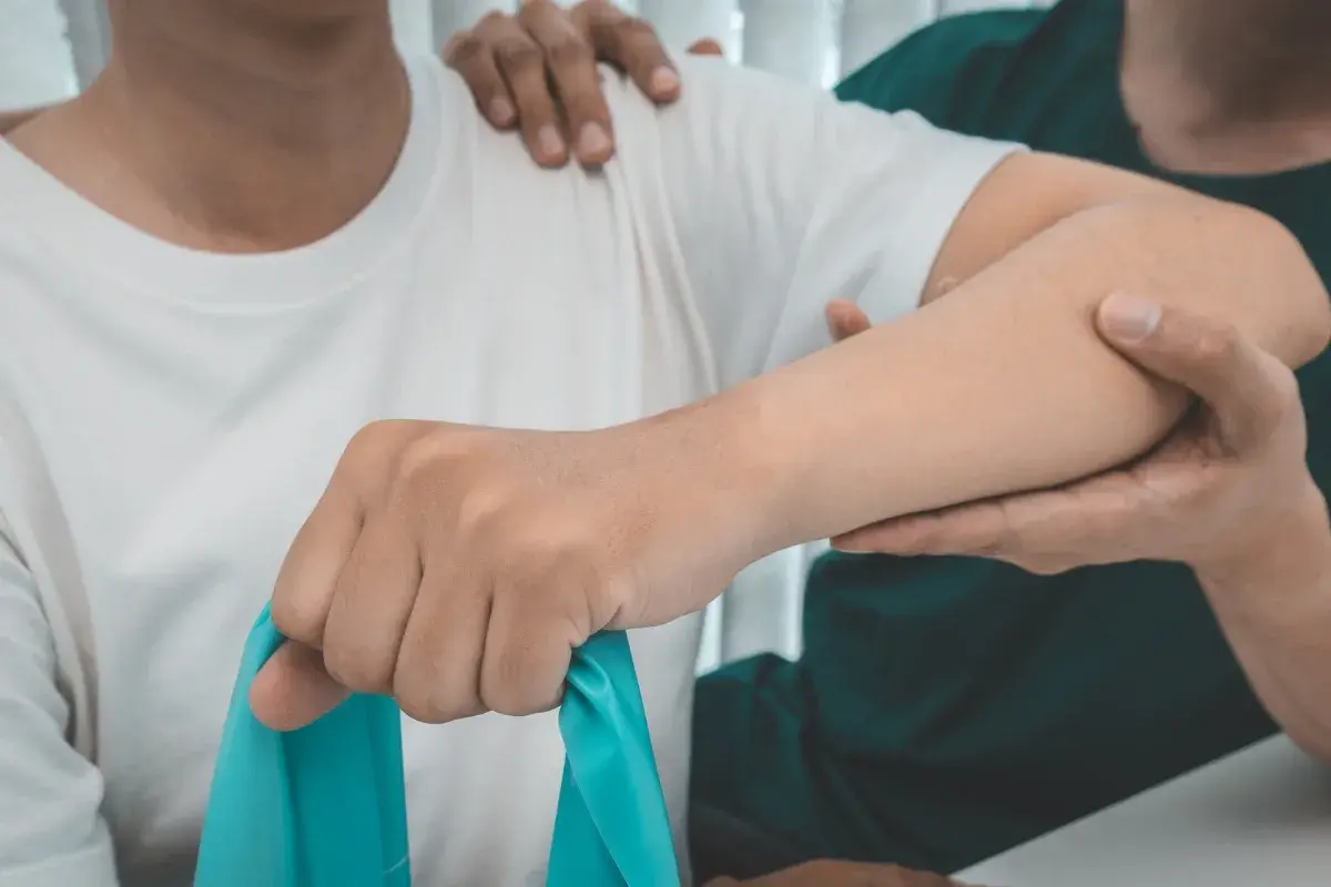Therapeut unterstützt bei Übungen für die liebscher und bracht schulter. Ein blaues Theraband wird genutzt.