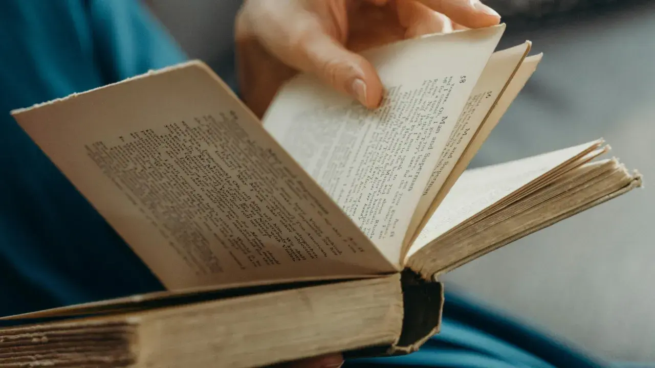 Eine Hand blättert in einem alten Buch. Der Titel "Man and Superman" ist sichtbar. Ein guter historischer Roman zum Eintauchen.