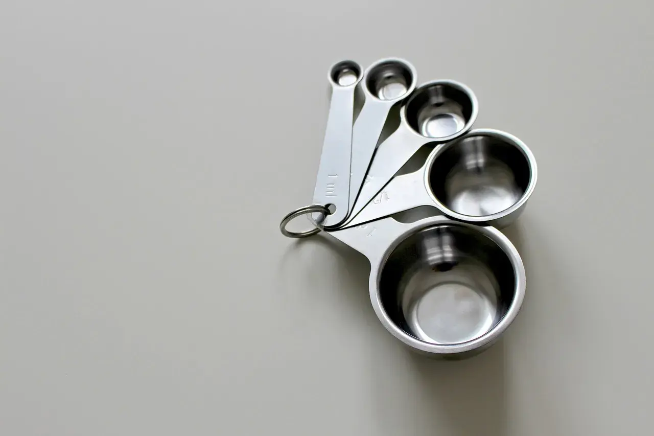 Zestaw metalowych miarek kuchennych o różnych rozmiarach, ułożonych na jasnym tle.