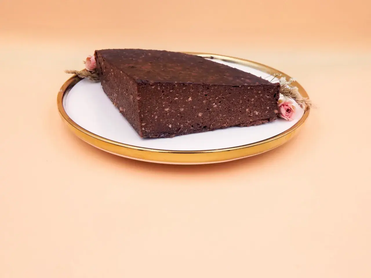 Czekoladowy brownie z bananami i masłem orzechowym, ozdobione suszonymi kwiatami, na talerzu ze złotym rantem.