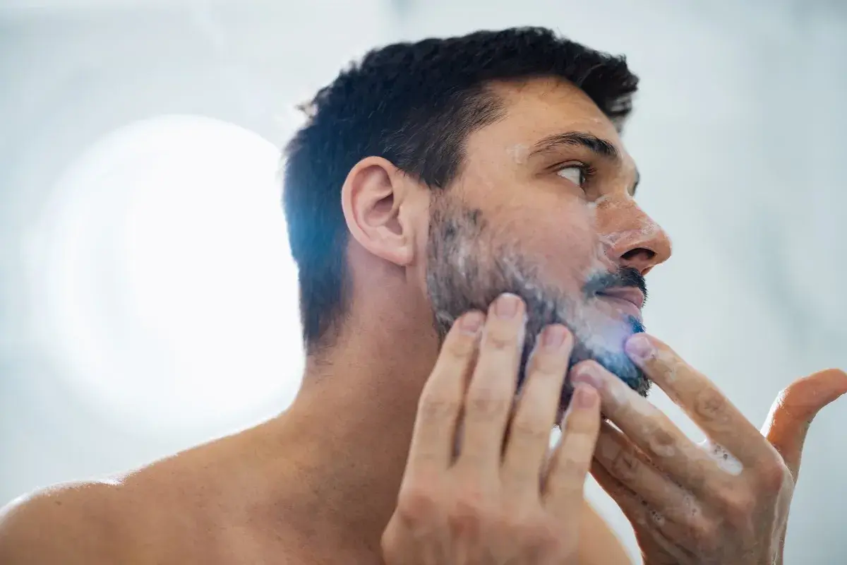 La cara de hombre con espuma de afeitar, preparándose para un afeitado apurado.