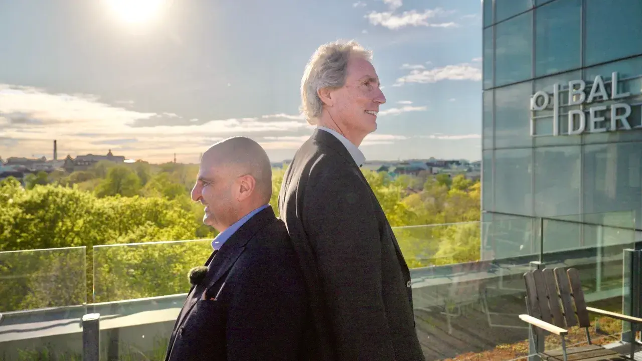Erik Selin och en kollega står rygg mot rygg på en takterrass med utsikt över en grönskande stad.