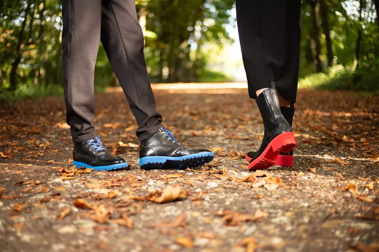 Deux paires de chaussures sur un sentier automnal. L'une a une semelle gomme ou caoutchouc bleue vive, l'autre une semelle rouge éclatante.