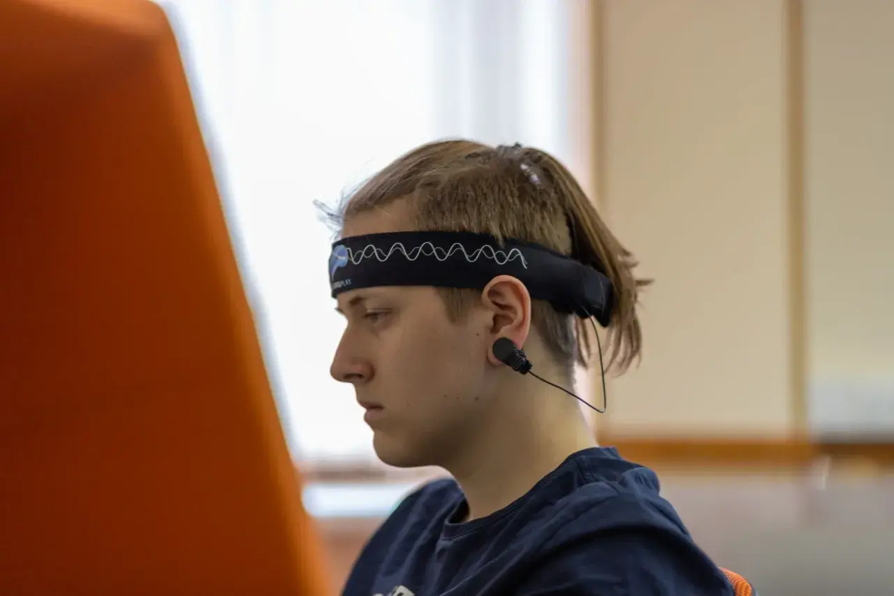Młody mężczyzna w opasce z elektrodami do eeg w czuwaniu, skupiony na czymś poza kadrem.
