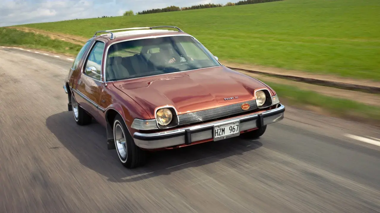 En brun AMC Pacer SC kör på en landsväg, med gröna fält som sträcker sig längs vägen.