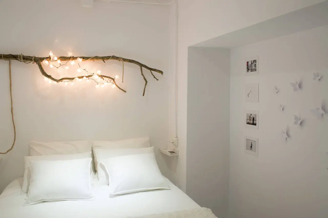 Ideas para decorar ramas secas: una rama con luces cálidas sobre la cama, fotos y mariposas en la pared.