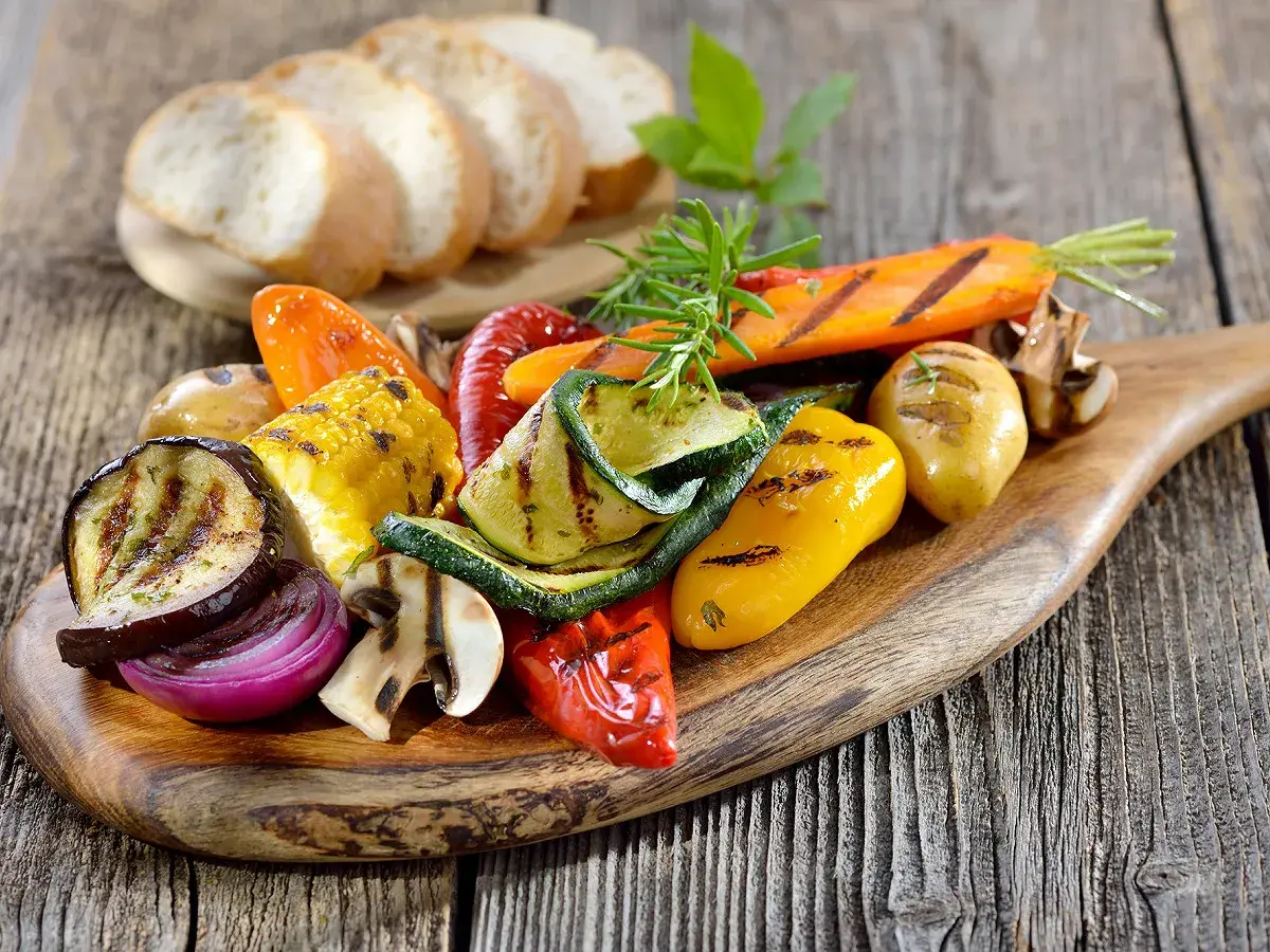 Légumes grillés colorés sur une planche en bois, accompagnés de pain frais. Un filet de crème de balsamique sublimerait ce plat.