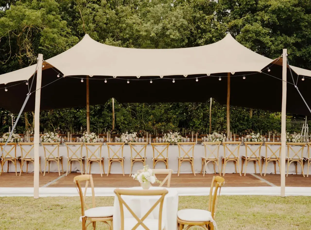 Une réception de mariage sous tente, avec des tables dressées et des chaises en bois. Un travail de cout wedding planner pour un événement mémorable.