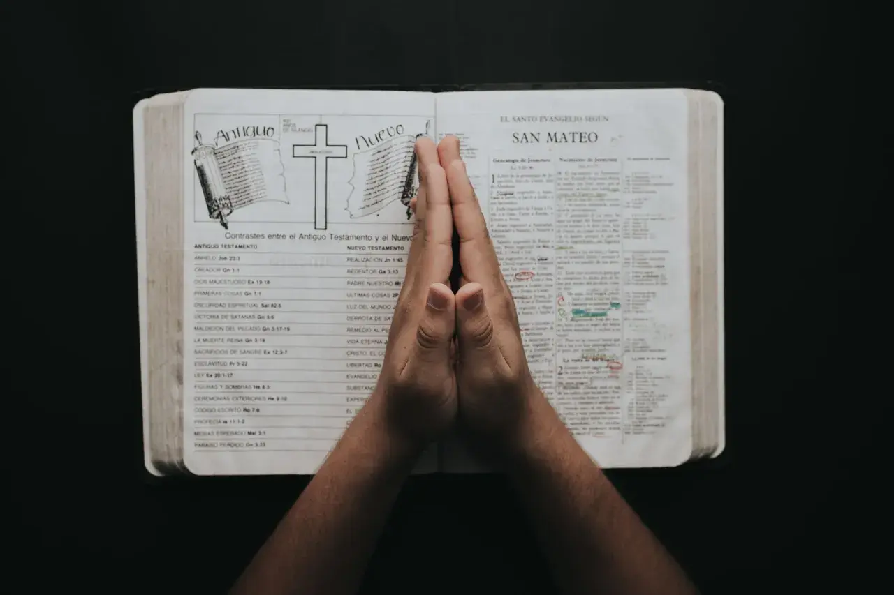 Dłonie złożone w geście modlitwy o prośbę nad otwartą Biblią.