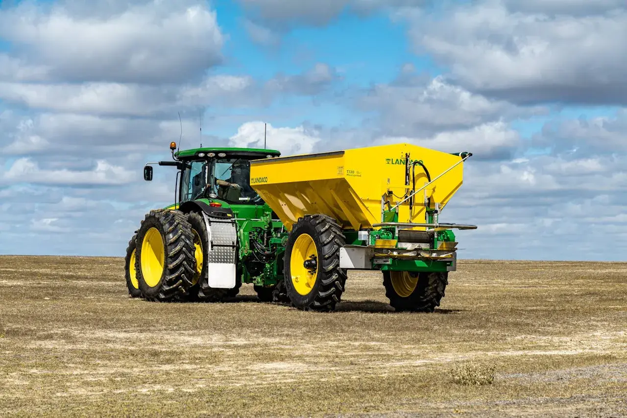 Zielony John Deere 7810 z żółtym rozsiewaczem Landaco T130 na polu.