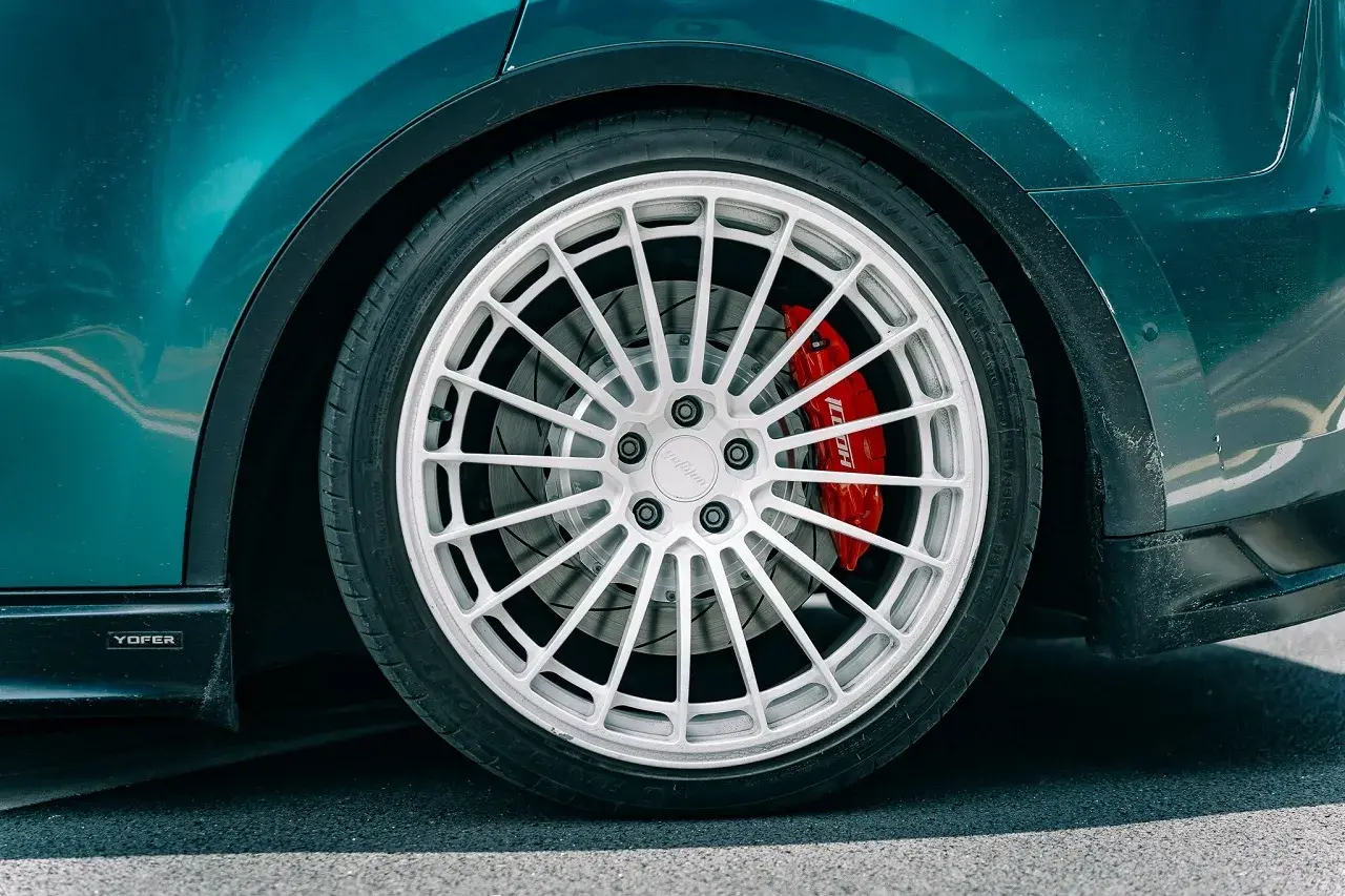 Detailaufnahme eines Autos mit auffälliger roter Bremsanlage. Der **Bremskolben fest** im Sattel deutet auf eine sportliche Performance hin.