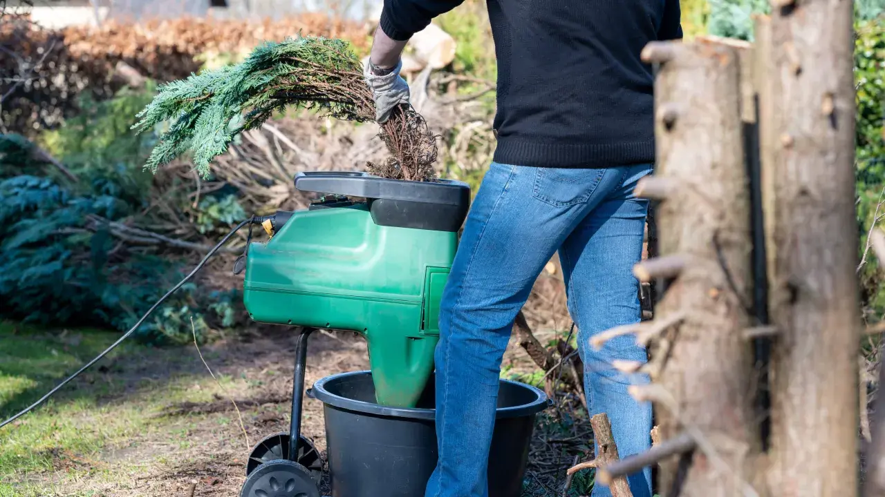 Gartenarbeit: Ein Mann zerkleinert mit einem Häcksler Zweige, um die **Kosten für Heckenentfernung** zu senken.