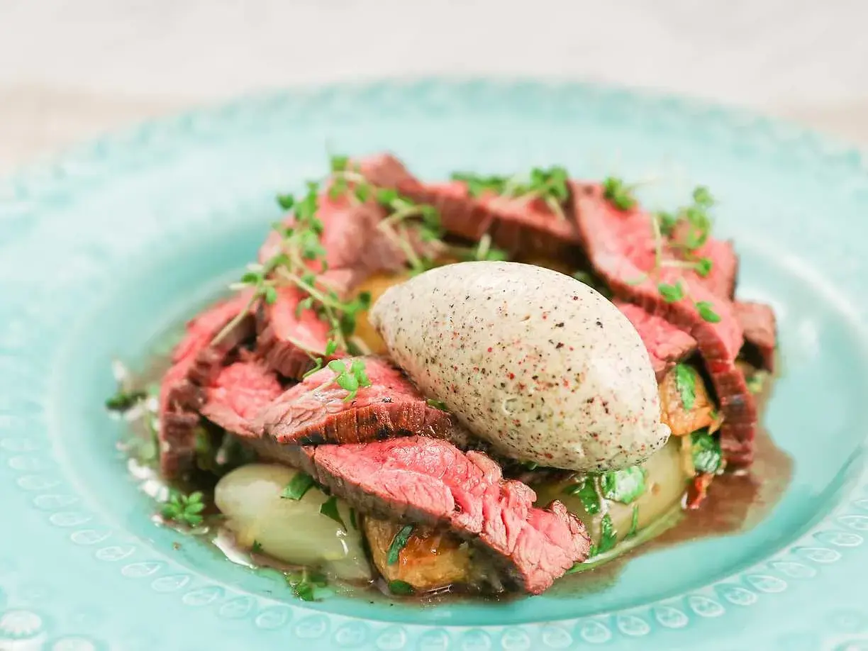 Skivad flankstek Morberg med potatis och en klick potatispuré, garnerad med örter.