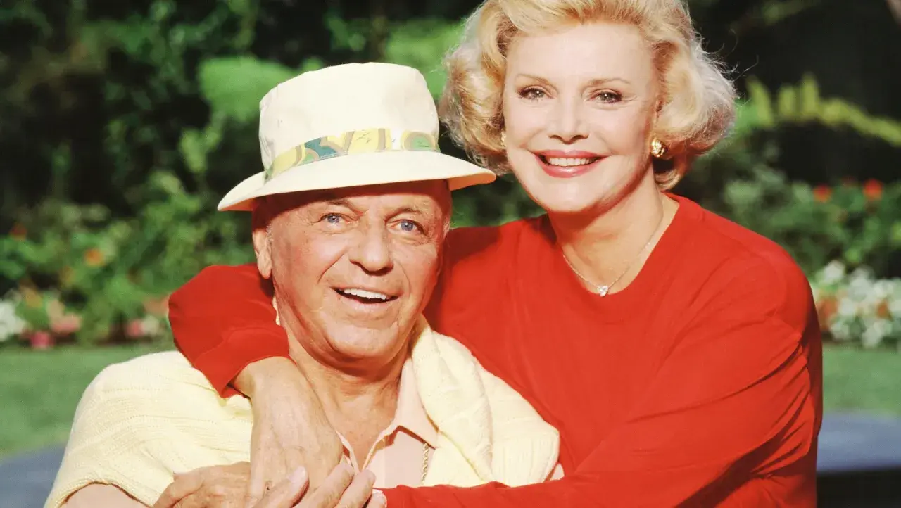Frank Sinatra z żoną Barbarą, uśmiechnięci, w słoneczny dzień na tle zieleni.
